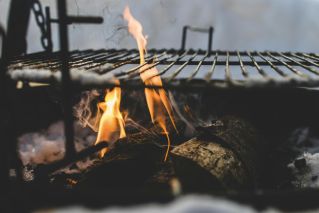 Close-up view of firewood burning in a fire pit with a metal grill above, outdoor setting.